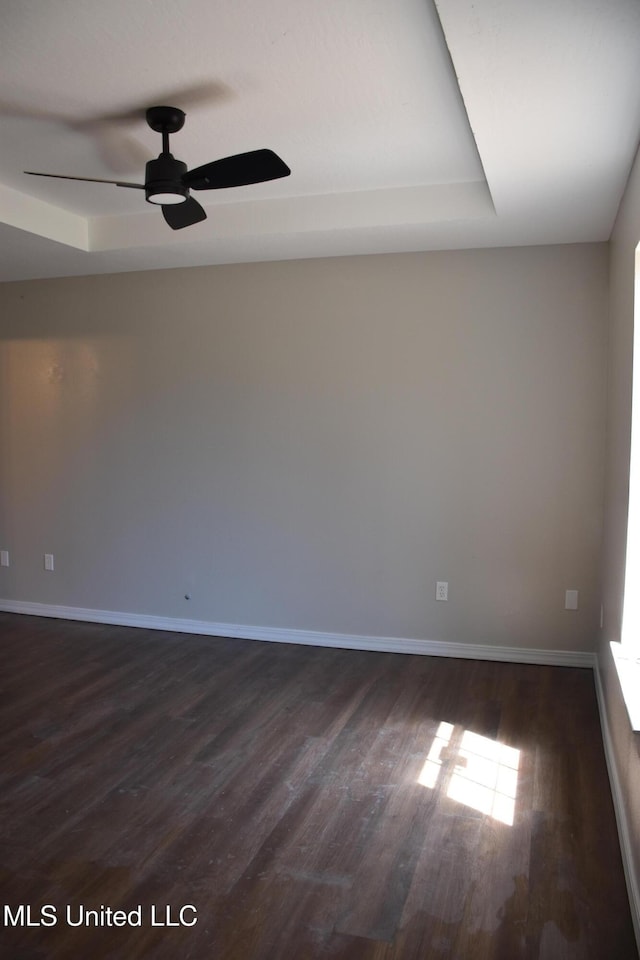 spare room featuring baseboards, dark wood-style floors, and a ceiling fan