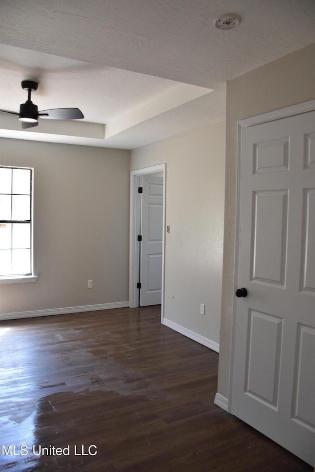 spare room with ceiling fan, a tray ceiling, baseboards, and dark wood-style flooring