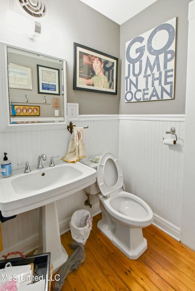 half bath featuring a wainscoted wall, wood finished floors, and toilet