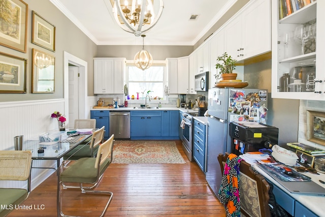 kitchen featuring blue cabinetry, an inviting chandelier, stainless steel appliances, a wainscoted wall, and a sink