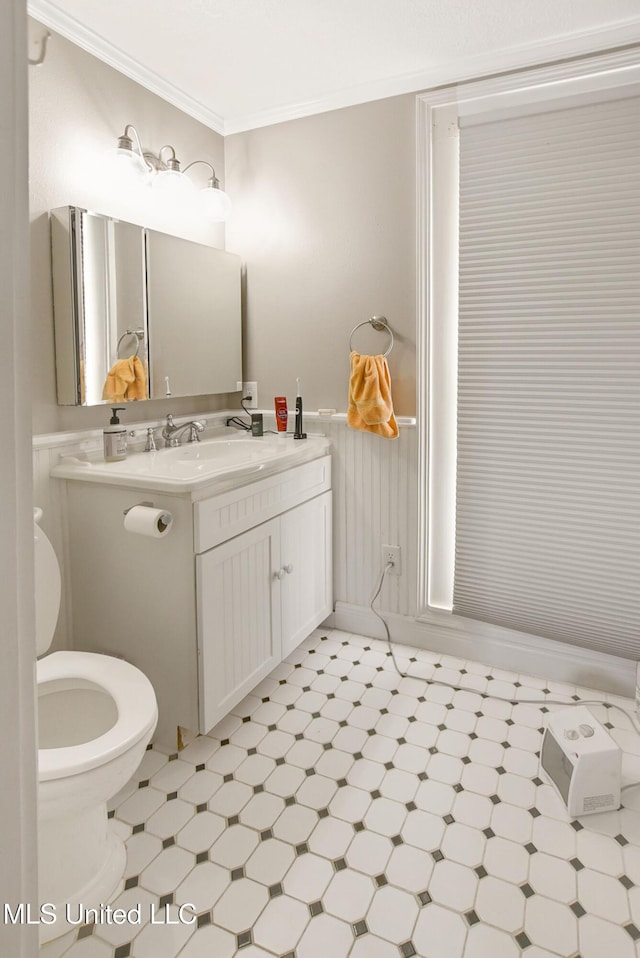 half bathroom featuring a wainscoted wall, ornamental molding, toilet, tile patterned floors, and vanity