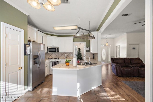 kitchen with tile countertops, white cabinets, sink, ornamental molding, and appliances with stainless steel finishes