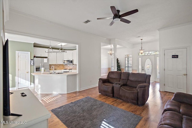 living room featuring ceiling fan with notable chandelier, wood-type flooring, ornamental molding, and sink