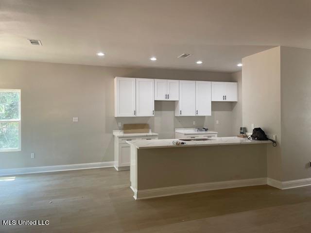 kitchen with wood-type flooring, kitchen peninsula, and white cabinets