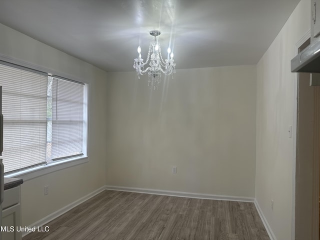 empty room featuring a notable chandelier, dark wood-type flooring, and baseboards