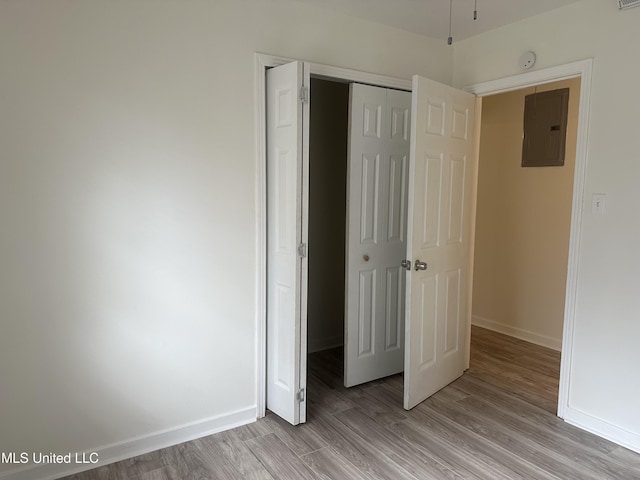 unfurnished bedroom with electric panel, a closet, baseboards, and light wood-style flooring