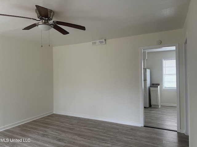 spare room with a ceiling fan, visible vents, baseboards, and dark wood-style flooring