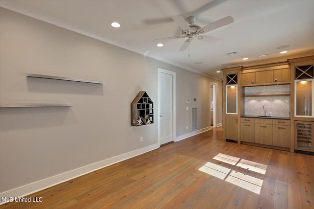 unfurnished living room with crown molding, wine cooler, hardwood / wood-style flooring, and ceiling fan