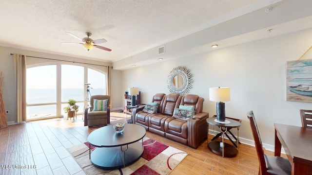 living room with crown molding, a water view, a textured ceiling, light hardwood / wood-style floors, and ceiling fan