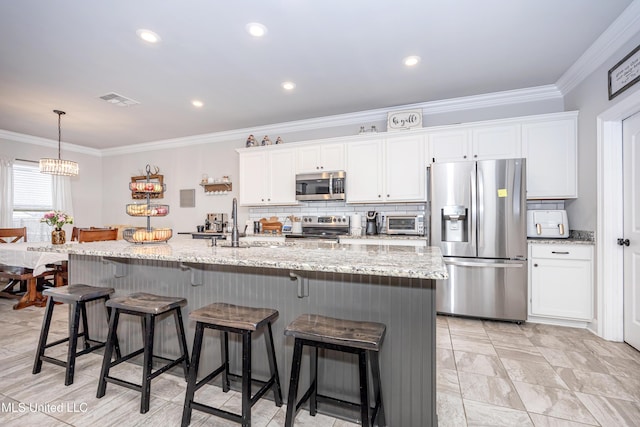 kitchen featuring a breakfast bar area, appliances with stainless steel finishes, light stone countertops, white cabinets, and a center island with sink