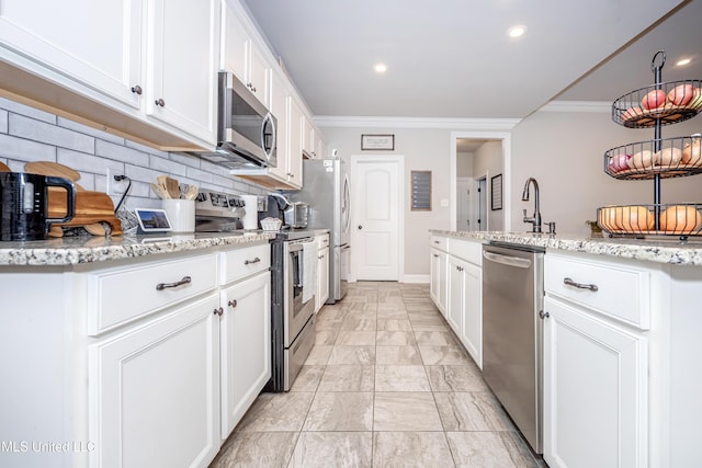 kitchen with white cabinetry, appliances with stainless steel finishes, ornamental molding, and light stone counters