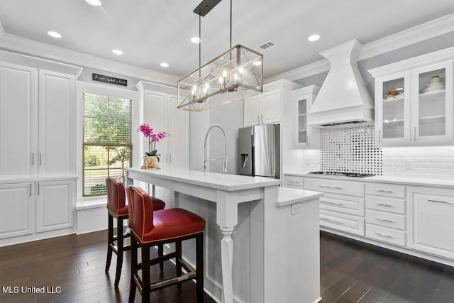 kitchen featuring premium range hood, gas cooktop, stainless steel refrigerator with ice dispenser, a kitchen island, and white cabinets