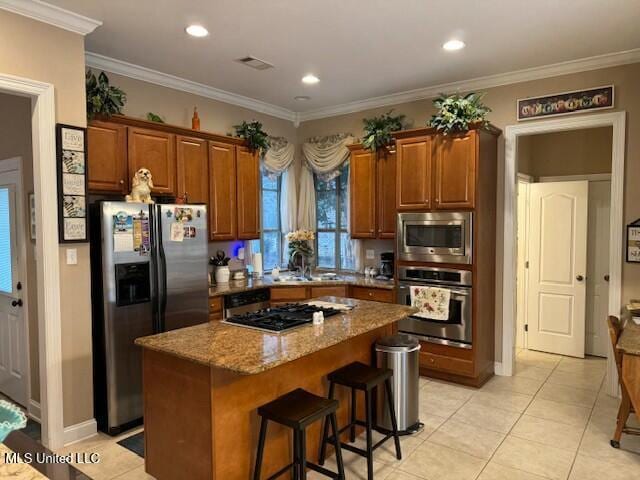 kitchen with appliances with stainless steel finishes, a center island, ornamental molding, light tile patterned flooring, and light stone counters