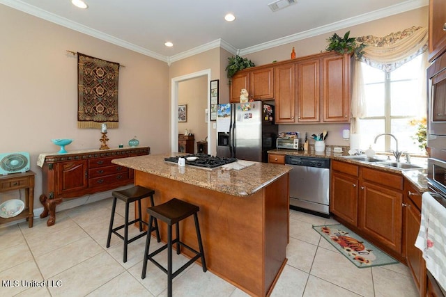 kitchen with appliances with stainless steel finishes, sink, a center island, light tile patterned floors, and light stone counters