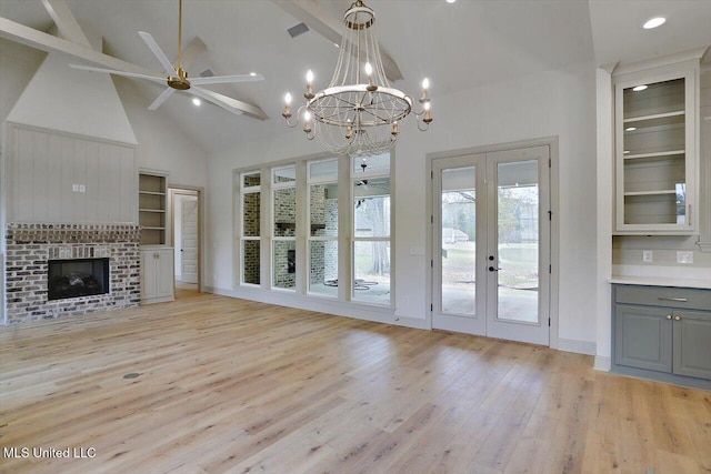 unfurnished living room with french doors, ceiling fan with notable chandelier, high vaulted ceiling, a fireplace, and light hardwood / wood-style floors