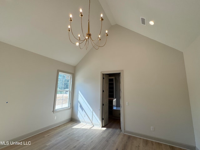 empty room featuring an inviting chandelier, high vaulted ceiling, and light wood-type flooring