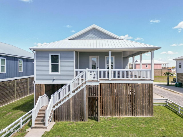 coastal home with fence, stairway, a porch, a front yard, and metal roof