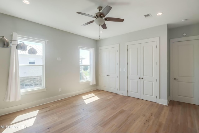 unfurnished bedroom with visible vents, light wood finished floors, baseboards, recessed lighting, and two closets