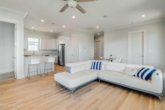 living area featuring recessed lighting, visible vents, light wood-style flooring, and ornamental molding