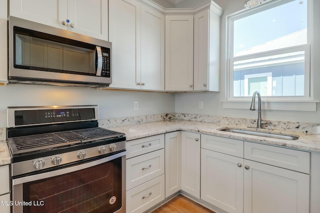 kitchen featuring a sink, light stone counters, appliances with stainless steel finishes, and white cabinets