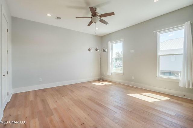 spare room featuring light wood-type flooring, visible vents, baseboards, and a healthy amount of sunlight