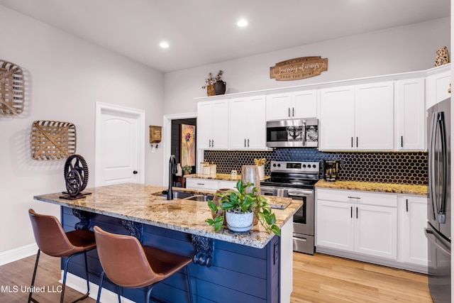 18109 Evergreen Dr, Gulfport, MS 39503 - kitchen featuring stainless steel appliances, a center island with sink, white cabinetry, a breakfast bar area, and light stone counters