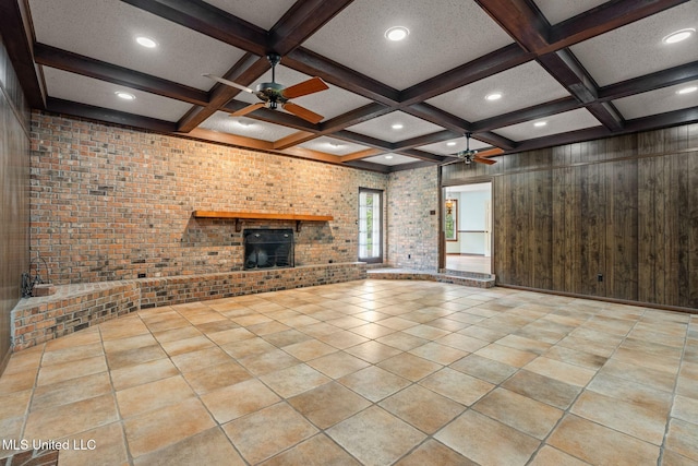 unfurnished living room with brick wall, a brick fireplace, beam ceiling, coffered ceiling, and ceiling fan