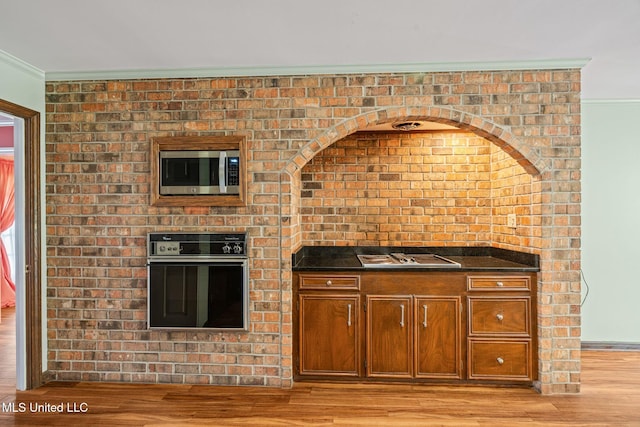 kitchen with ornamental molding, brown cabinets, stainless steel microwave, light wood finished floors, and black oven