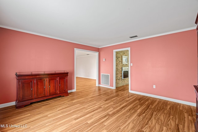 spare room with light wood finished floors, visible vents, crown molding, and a brick fireplace