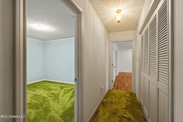 hallway with a textured ceiling, baseboards, and carpet floors