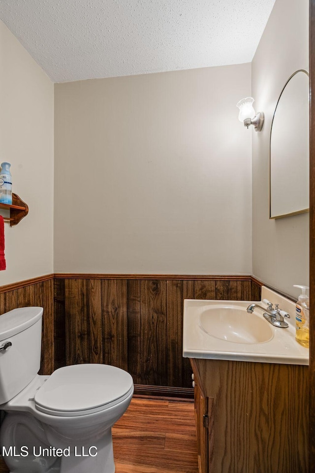 bathroom featuring a textured ceiling, vanity, a wainscoted wall, toilet, and wooden walls