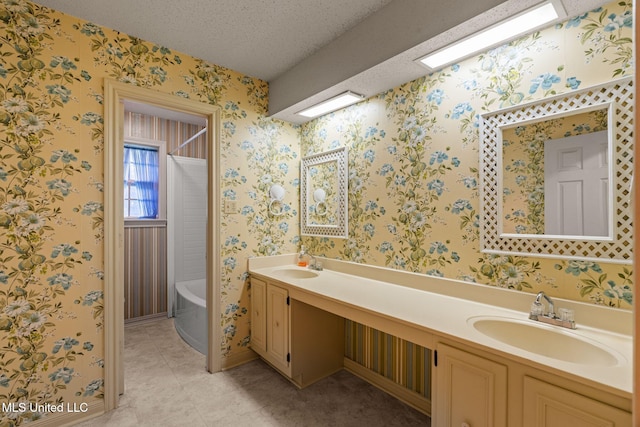 full bath with a sink, a bathing tub, a textured ceiling, and wallpapered walls