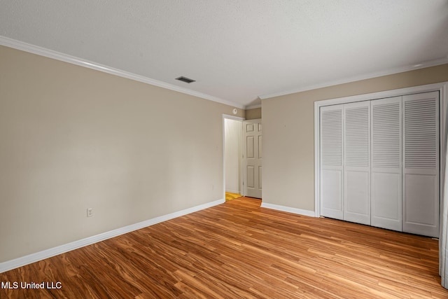 unfurnished bedroom featuring light wood-style floors, a closet, ornamental molding, visible vents, and baseboards
