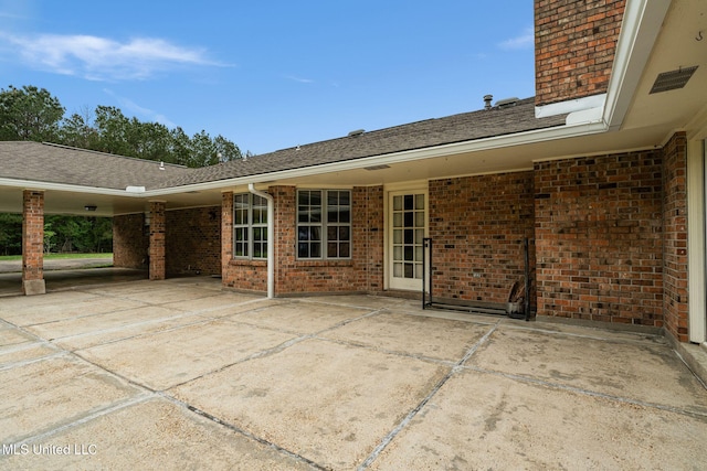 rear view of house featuring brick siding, a patio, and roof with shingles