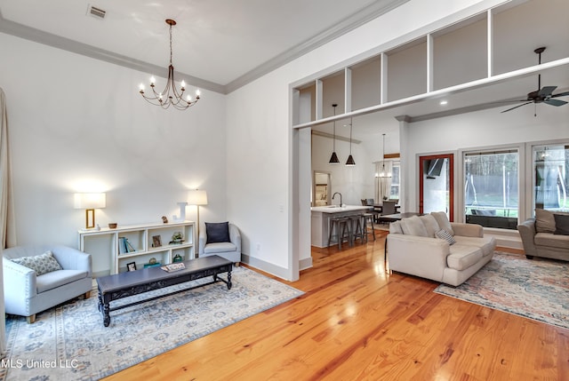 living room with ceiling fan with notable chandelier, a high ceiling, ornamental molding, and light wood-type flooring