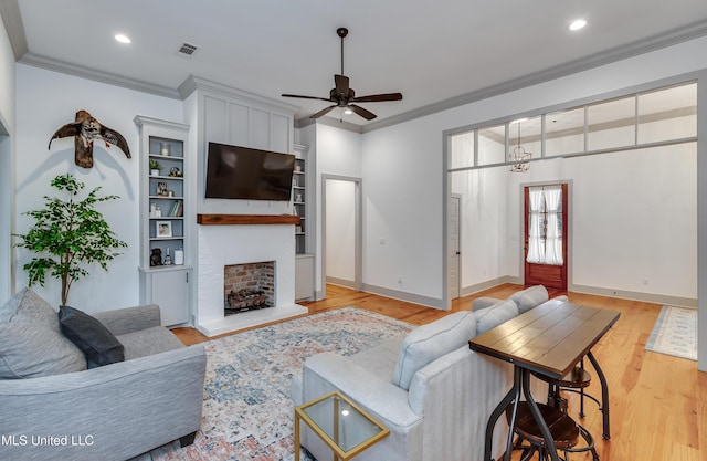 living room featuring ceiling fan, a large fireplace, light wood-type flooring, built in features, and ornamental molding