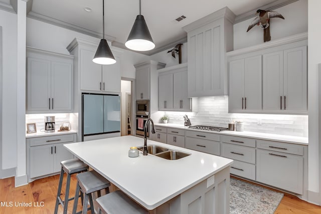 kitchen featuring an island with sink, stainless steel appliances, tasteful backsplash, pendant lighting, and sink