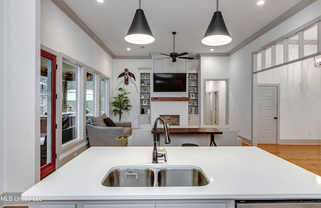 kitchen featuring ornamental molding, sink, hanging light fixtures, and an island with sink