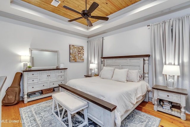 bedroom with ceiling fan, light wood-type flooring, a tray ceiling, and ornamental molding