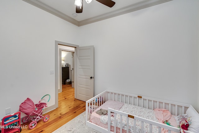 bedroom featuring ceiling fan, a nursery area, ornamental molding, and hardwood / wood-style floors