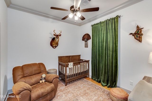 bedroom featuring ceiling fan, crown molding, and a crib