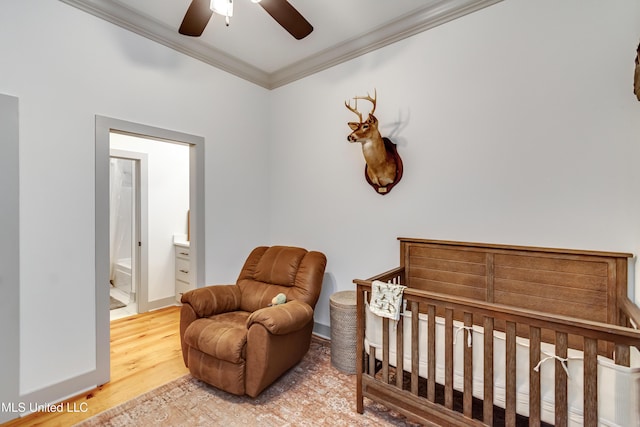 bedroom featuring hardwood / wood-style flooring, a crib, ceiling fan, ensuite bath, and ornamental molding