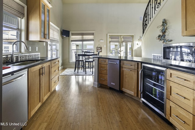 kitchen with stainless steel appliances, dark countertops, beverage cooler, and a sink