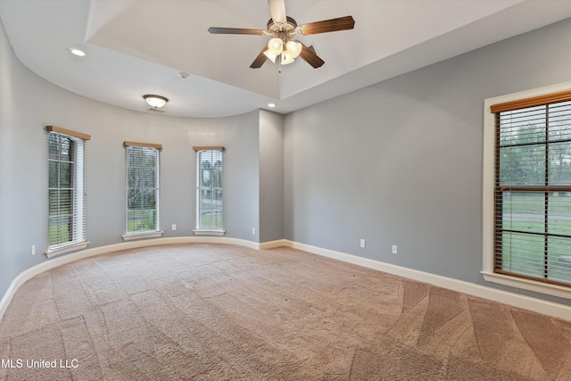 carpeted spare room featuring a tray ceiling and ceiling fan