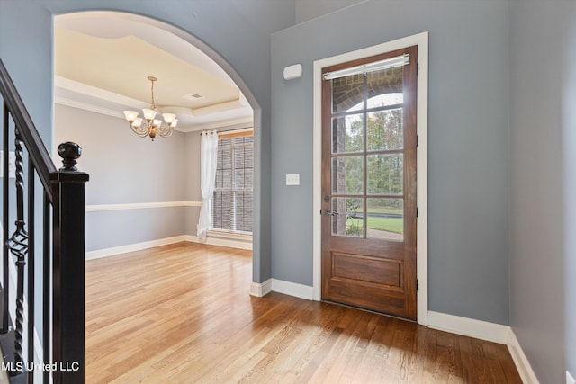 entryway with an inviting chandelier, a tray ceiling, and light hardwood / wood-style flooring