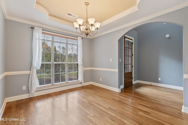 empty room featuring hardwood / wood-style floors, a tray ceiling, ornamental molding, and a notable chandelier