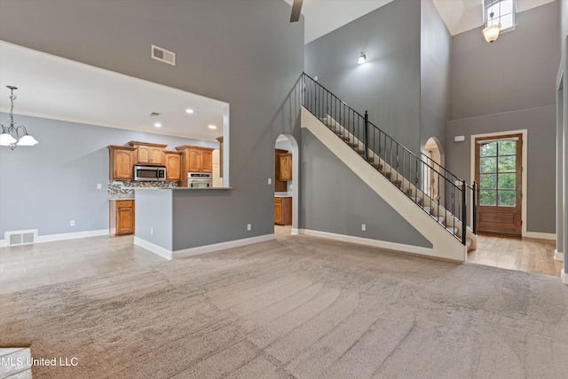 unfurnished living room with light carpet, a towering ceiling, and an inviting chandelier