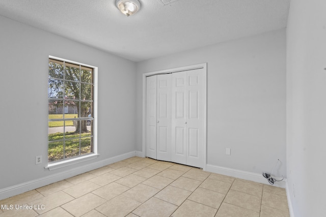 unfurnished bedroom with multiple windows, a closet, light tile patterned flooring, and a textured ceiling