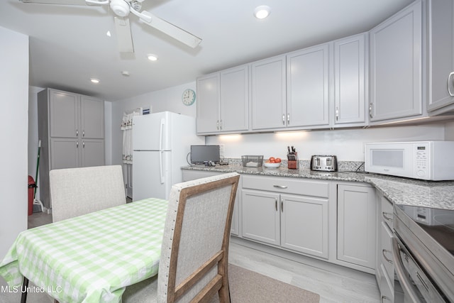 kitchen with ceiling fan, light stone counters, white appliances, and light wood-type flooring