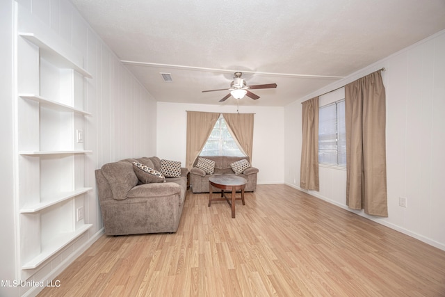 sitting room with ceiling fan, light hardwood / wood-style flooring, built in features, and a textured ceiling